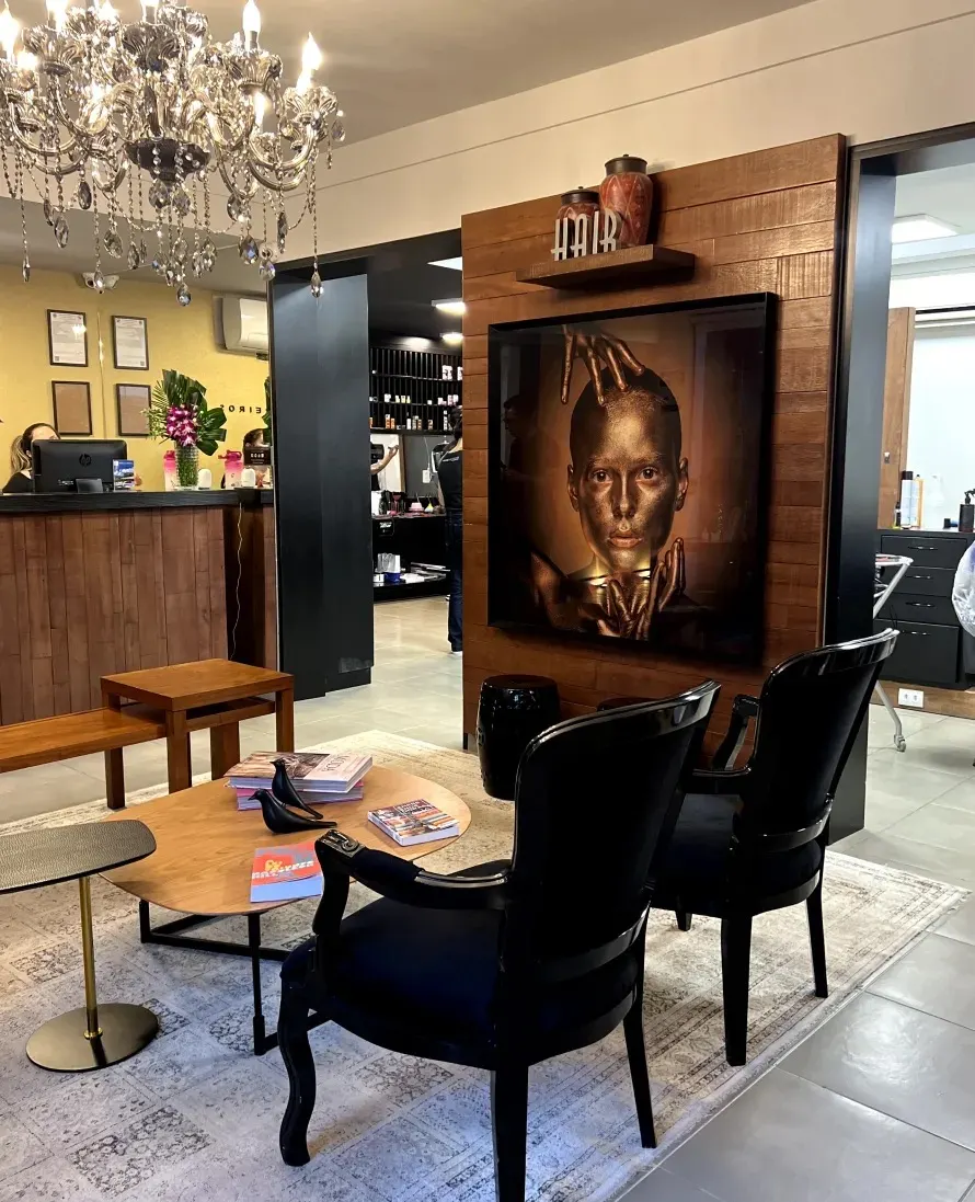 Recepção do salão Matsunos, com painel de madeira, quadro em tons dourados e poltronas pretas